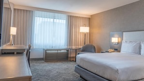 A hotel room with a bed, desk, chair, and a large window with curtains. - Orange County Hotel (Santa Ana)