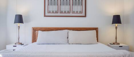 Un lit bien fait, avec une tête de lit en bois, deux tables de chevet avec des lampes et une œuvre d’art encadrée au-dessus du lit.
