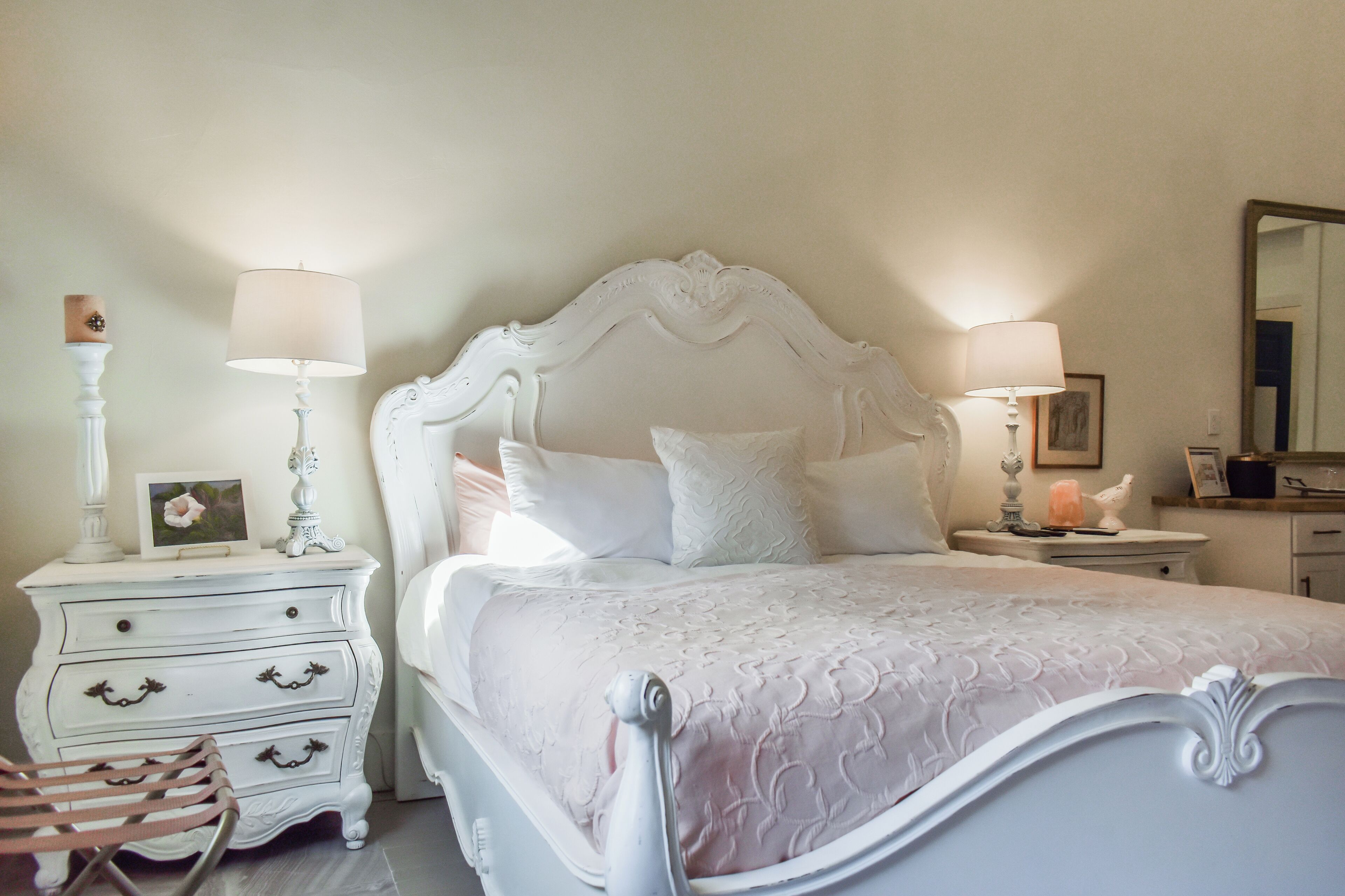 A bedroom with a white bed, two bedside tables, a chair, and a mirror on the wall.