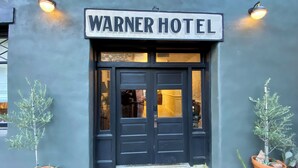 Het uiterlijk van Hotel Warner, met een donkere gevel, een bord boven de ingang en twee potplanten aan weerszijden.