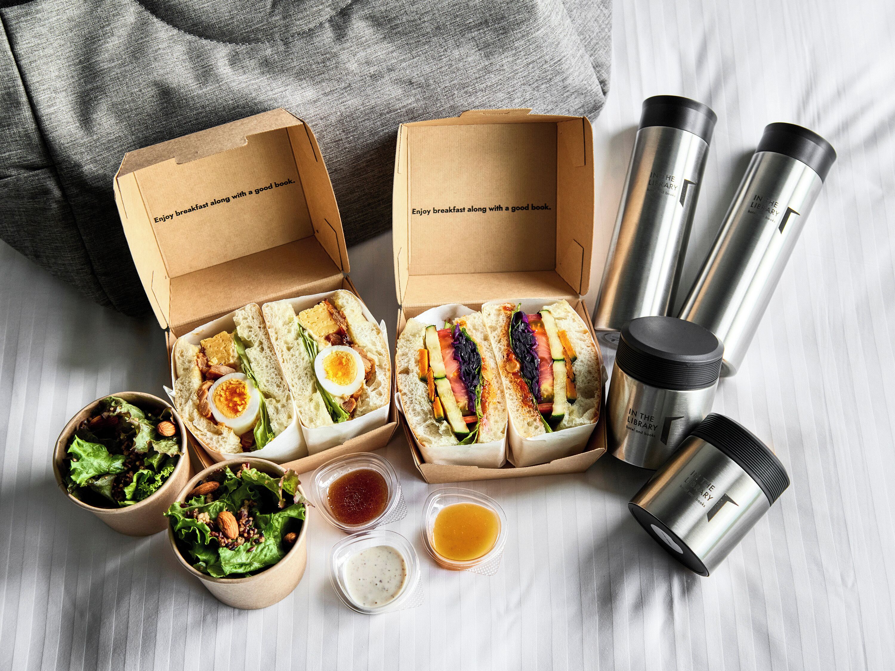 Two open lunch boxes with sandwiches, salad, and condiments on a table.