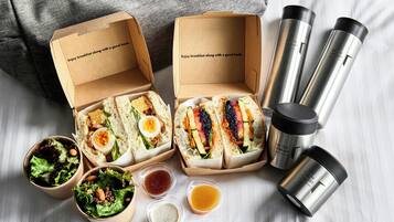 Two open lunch boxes with sandwiches, salad, and condiments on a table.