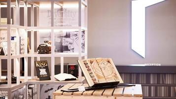 A reception area with a modern design, featuring a wooden desk with a laptop and a book, surrounded by shelves with books and a large illuminated 'T' sign.