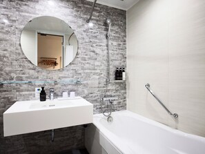 A modern bathroom with a white sink, a round mirror, a shower with a handheld showerhead, and a grab bar beside the bathtub. - IN THE LIBRARY hotel and books TOKOROZAWA (Tokorozawa)