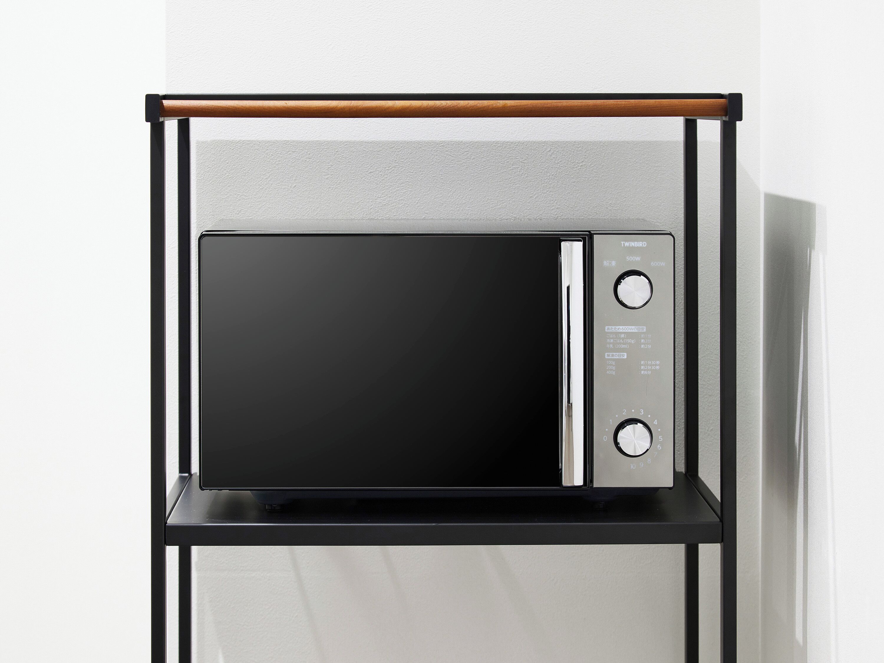 A microwave oven with a digital display and control panel, mounted on a black metal stand with a wooden top.