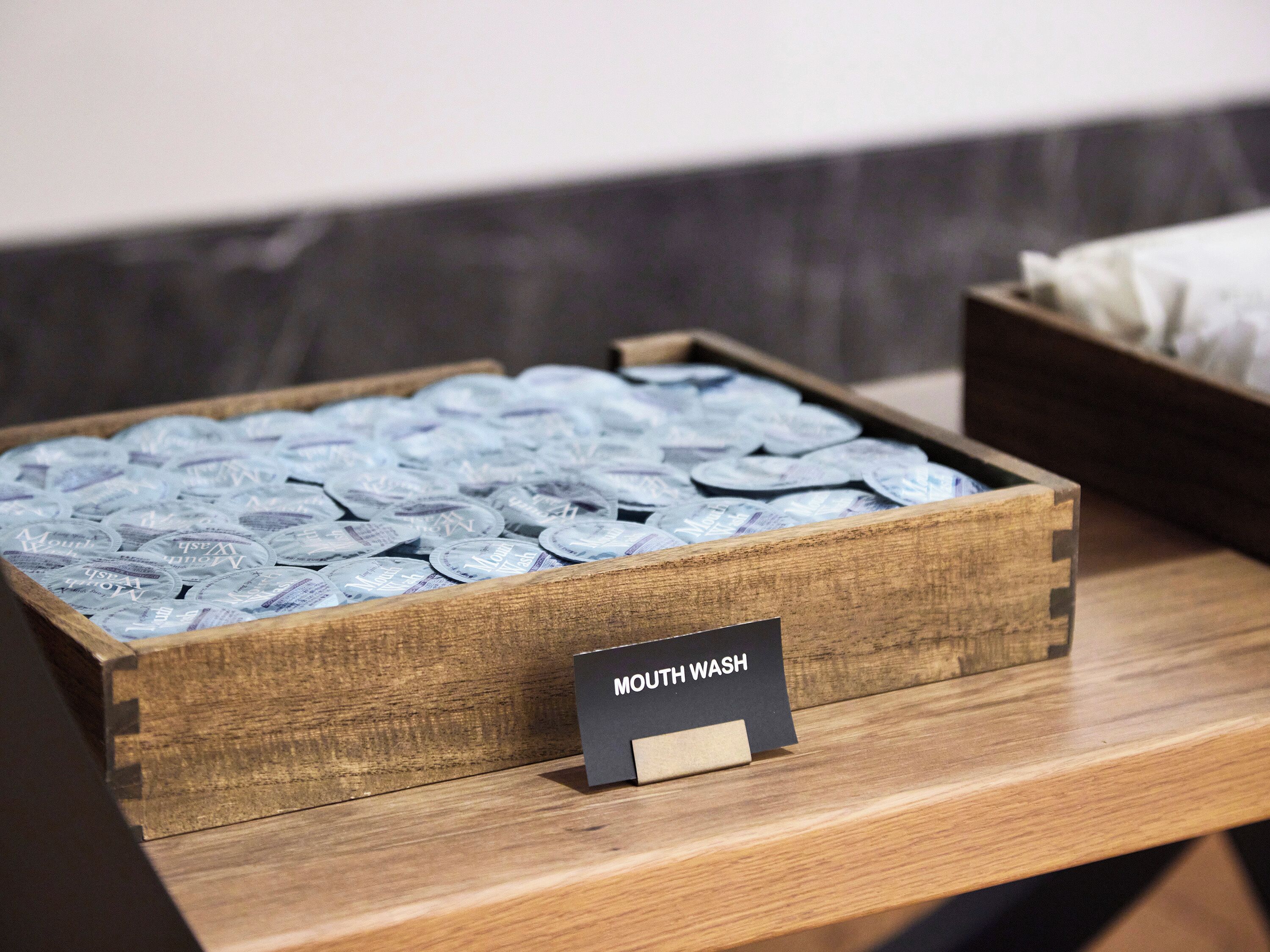 Una caja de madera llena de botellas de enjuague bucal etiquetadas como “Mouth Wash” sobre una mesa de madera.