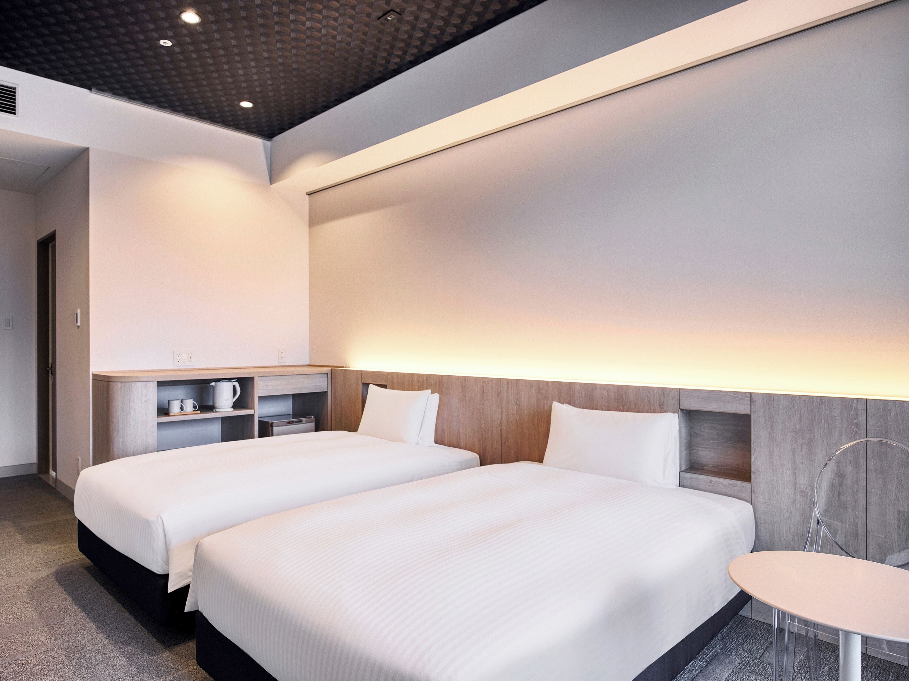 Ein modernes Hotelzimmer mit zwei Betten, einem kleinen Tisch und einer eingebauten Ablage mit einem Wasserkocher.