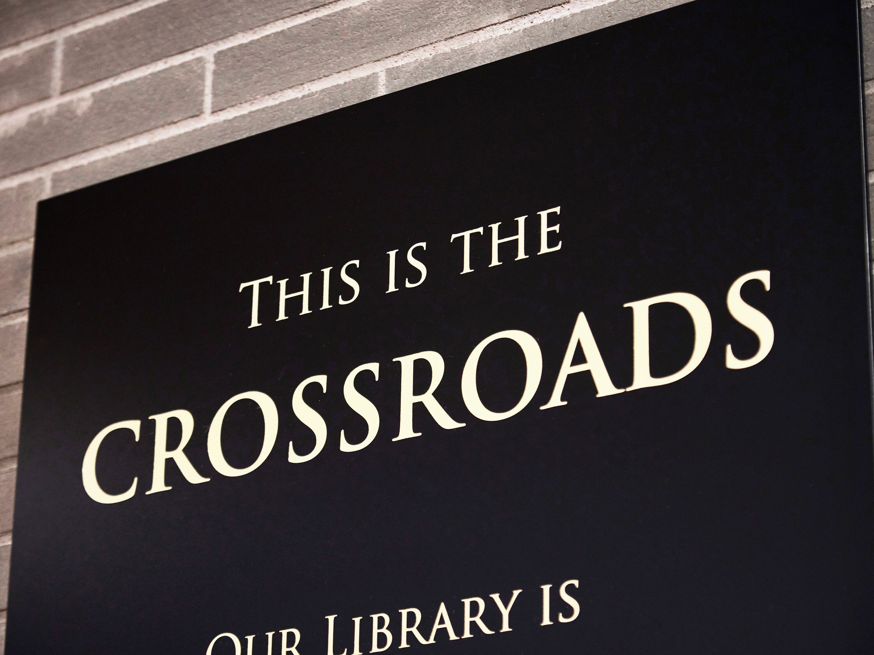 A sign with the text "THIS IS THE CROSSROADS OUR LIBRARY IS".