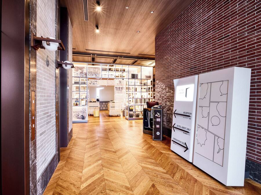 A hotel lobby with a wooden herringbone floor, brick walls, and a reception desk.
