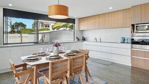 A modern kitchen with a dining area, large windows, and a view of the outdoors. - Beautiful Balook - 3 Bedroom Beach House (Lauderdale)