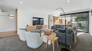 A modern living room with a flat-screen TV, grey sofas, a wooden coffee table, and a large window offering a view of the outdoors. - Beautiful Balook - 3 Bedroom Beach House (Lauderdale)