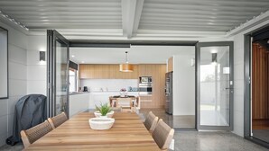 A modern kitchen with wooden cabinets, a stainless steel refrigerator, and a dining area with a wooden table and chairs. - Beautiful Balook - 3 Bedroom Beach House (Lauderdale)