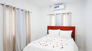 Habitación de hotel con cama, ropa de cama blanca, cabecero de madera y unidad de aire acondicionado en la pared.