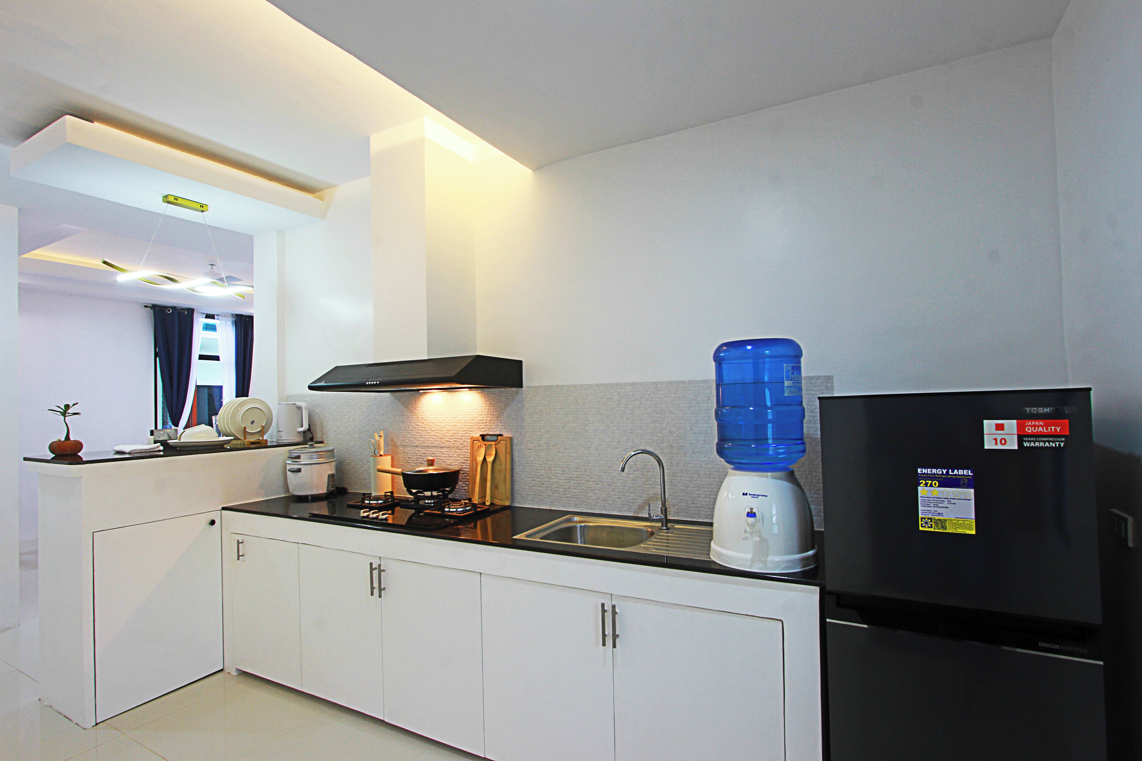 A modern kitchen with white cabinets, a black countertop, a built-in stove, a sink, and a refrigerator.