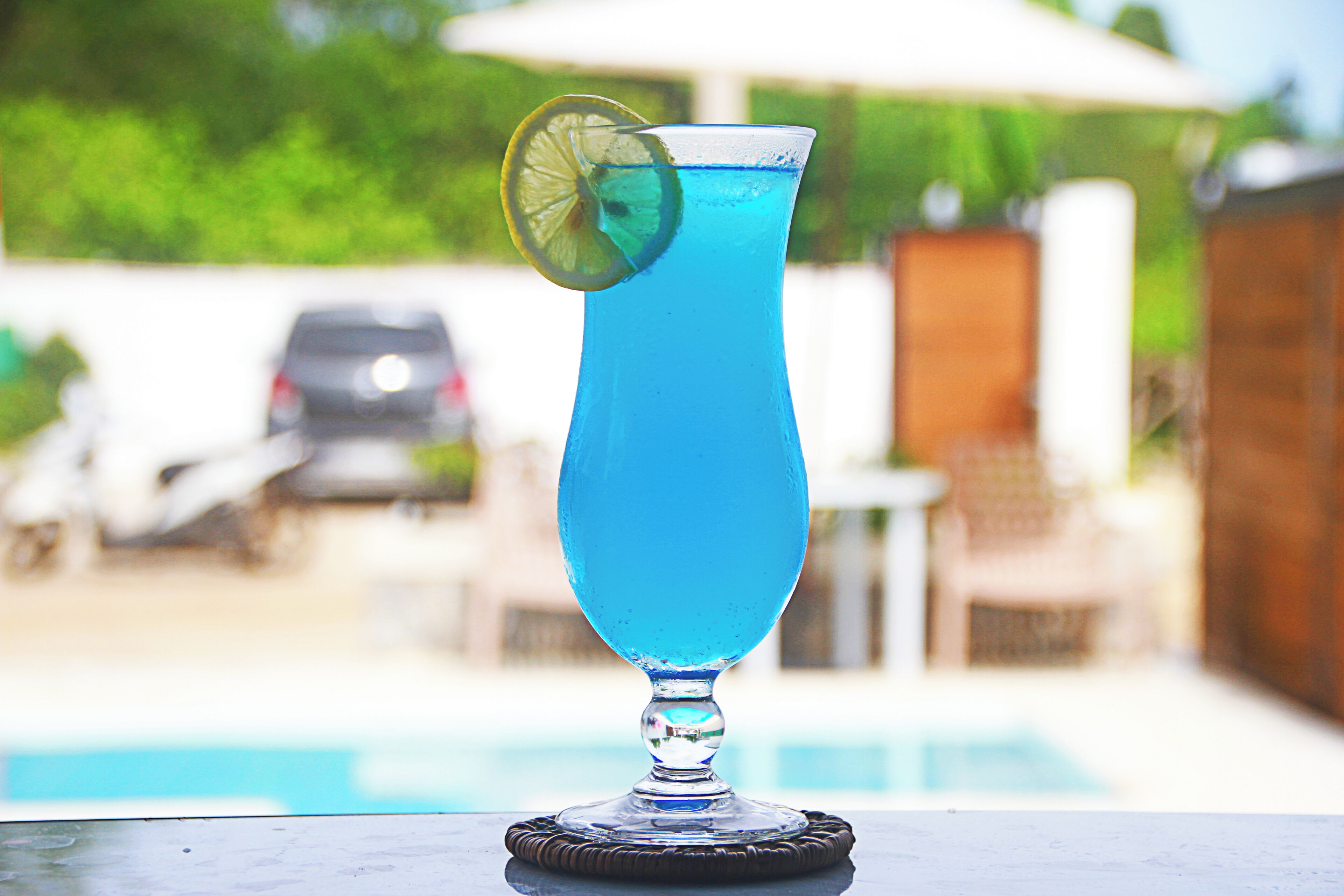 Ein blauer Cocktail mit Limettenscheibe auf einem Untersetzer in der Nähe eines Pools.