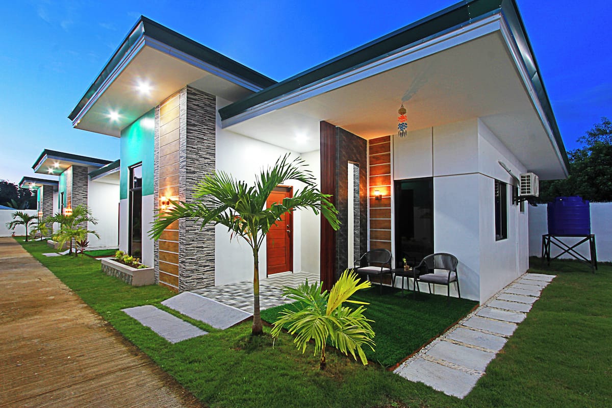 A modern house with a well-maintained lawn, a wooden pathway, and a patio with outdoor seating.