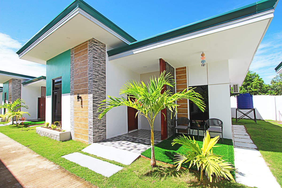 A modern house with a covered porch, a stone pillar, and a small garden with palm trees.