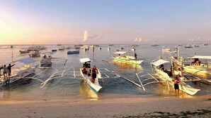 Une plage où plusieurs bateaux sont ancrés dans des eaux peu profondes, avec des personnes à bord et un ciel dégagé.