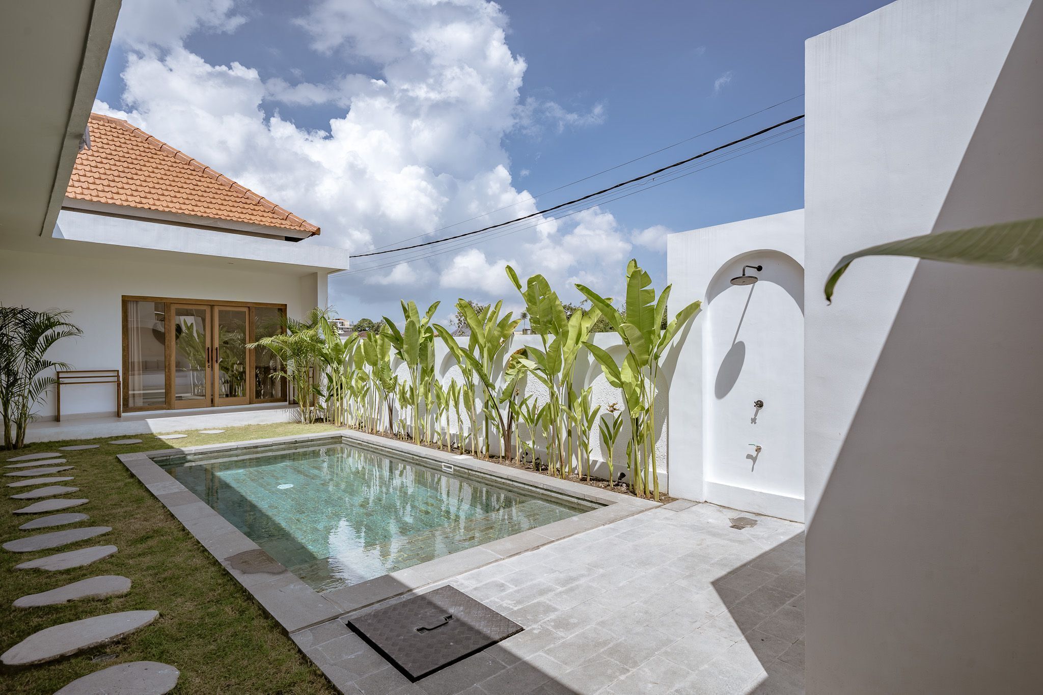 A modern house with a swimming pool, a tiled roof, and a garden with banana plants.