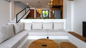 A modern living room with a sectional sofa, a wooden coffee table, and a staircase leading to an upper level. - Amal Villa By Betterplace (Canggu)