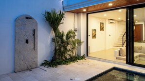 A modern house with a stone archway, a glass door leading to a living area with a staircase, and a small pool. - Amal Villa By Betterplace (Canggu)