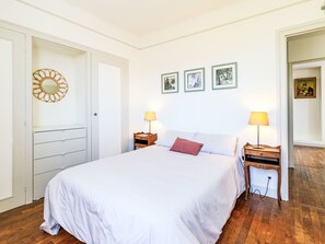 Un dormitorio con una cama grande, dos mesitas de noche con lámparas, un armario y tres cuadros enmarcados en la pared.