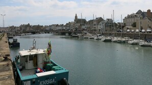 Un puerto con barcos amarrados, un paseo marítimo y edificios históricos al fondo.