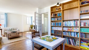 Un salón con piso de madera, un sofá blanco, una mesa de centro y una estantería llena de libros.