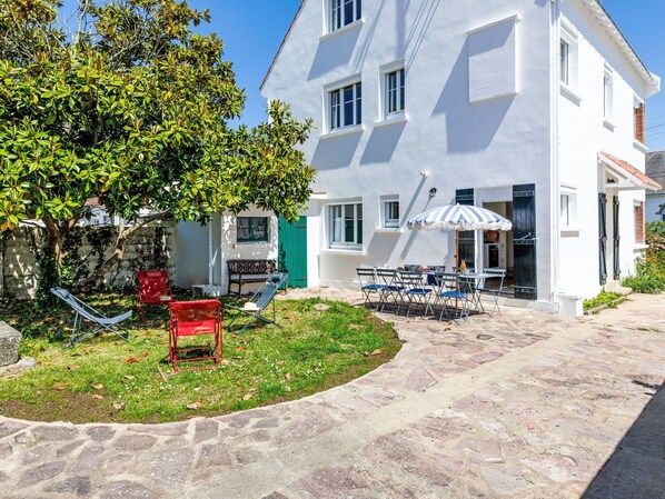 Un edificio blanco con un camino de piedra que lleva a un espacio de descanso con una mesa y sillas.