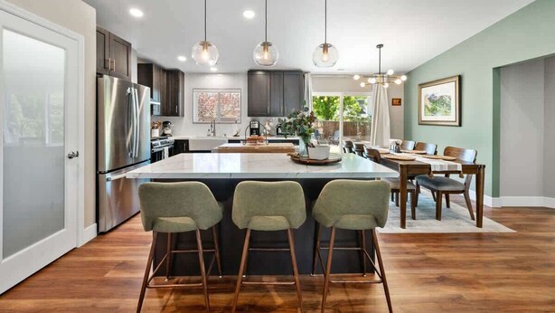 A modern kitchen with a central island, bar stools, stainless steel appliances, and pendant lighting.