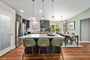 Cozinha moderna com ilha central, banquetas, eletrodomésticos de aço inoxidável e iluminação pendente.
