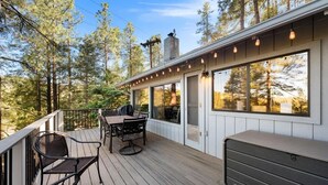 A wooden deck with a table and chairs, large windows, and a view of trees. - Prescott Pine Retreat | Views • Fireplace • Patio (Prescott)