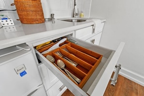 Cozinha com bancada branca, pia de aço inoxidável e organizador de gaveta com utensílios.