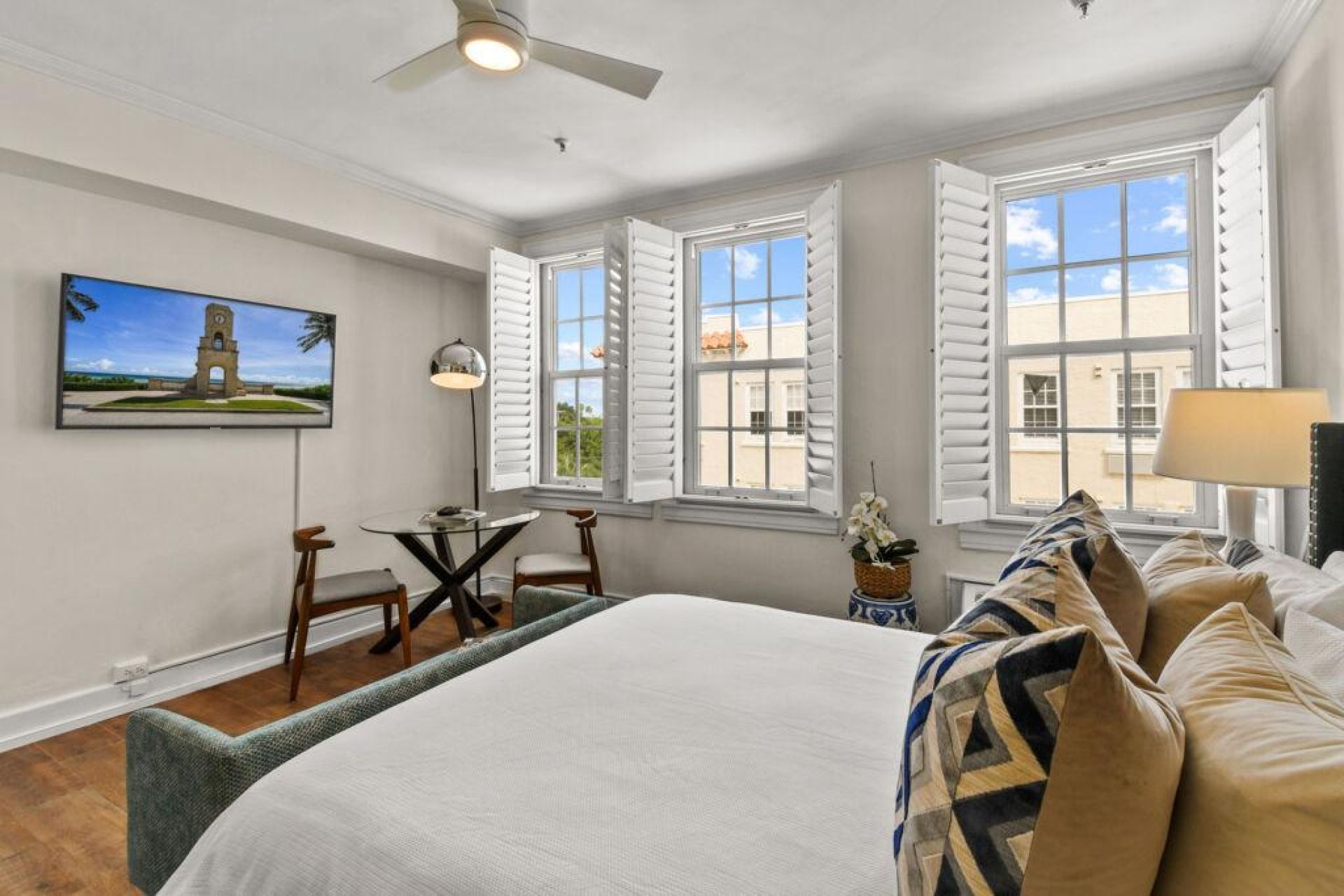 A hotel room with a bed, a desk, two chairs, a lamp, and a painting of a tower.