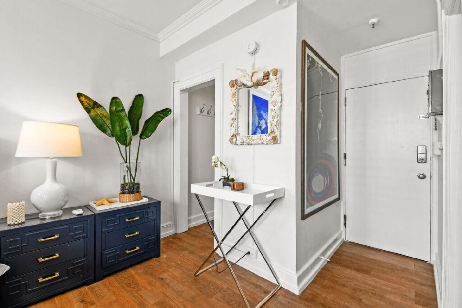 A room with a white console table, a potted plant, a mirror with a decorative frame, and a door with a circular glass window.
