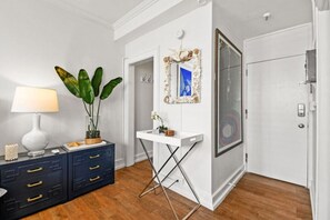 Een kamer met een witte console tafel, een potplant, een spiegel met decoratieve lijst, en een deur met een rond raam.
