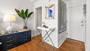Een kamer met een witte console tafel, een wit bureau, een grote spiegel en een deur met een ruit.