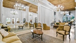 Een ruime lobby met hoge plafonds, kroonluchters en diverse zithoeken, waaronder banken en fauteuils.