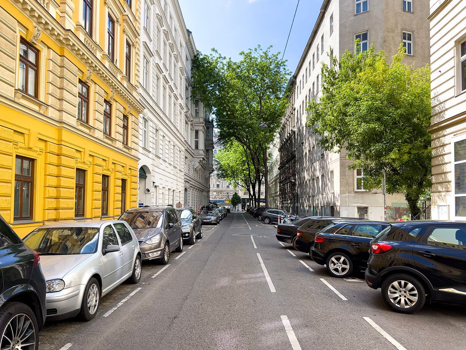 Una calle bordeada de vehículos estacionados y edificios.
