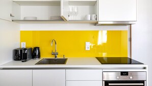 Une cuisine moderne avec des meubles blancs, un pare-feu jaune, un évier en acier inoxydable et un four encastré.