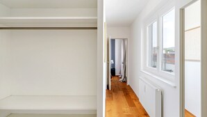 Une pièce aux murs blancs, avec un plancher en bois et une fenêtre donnant sur des immeubles.