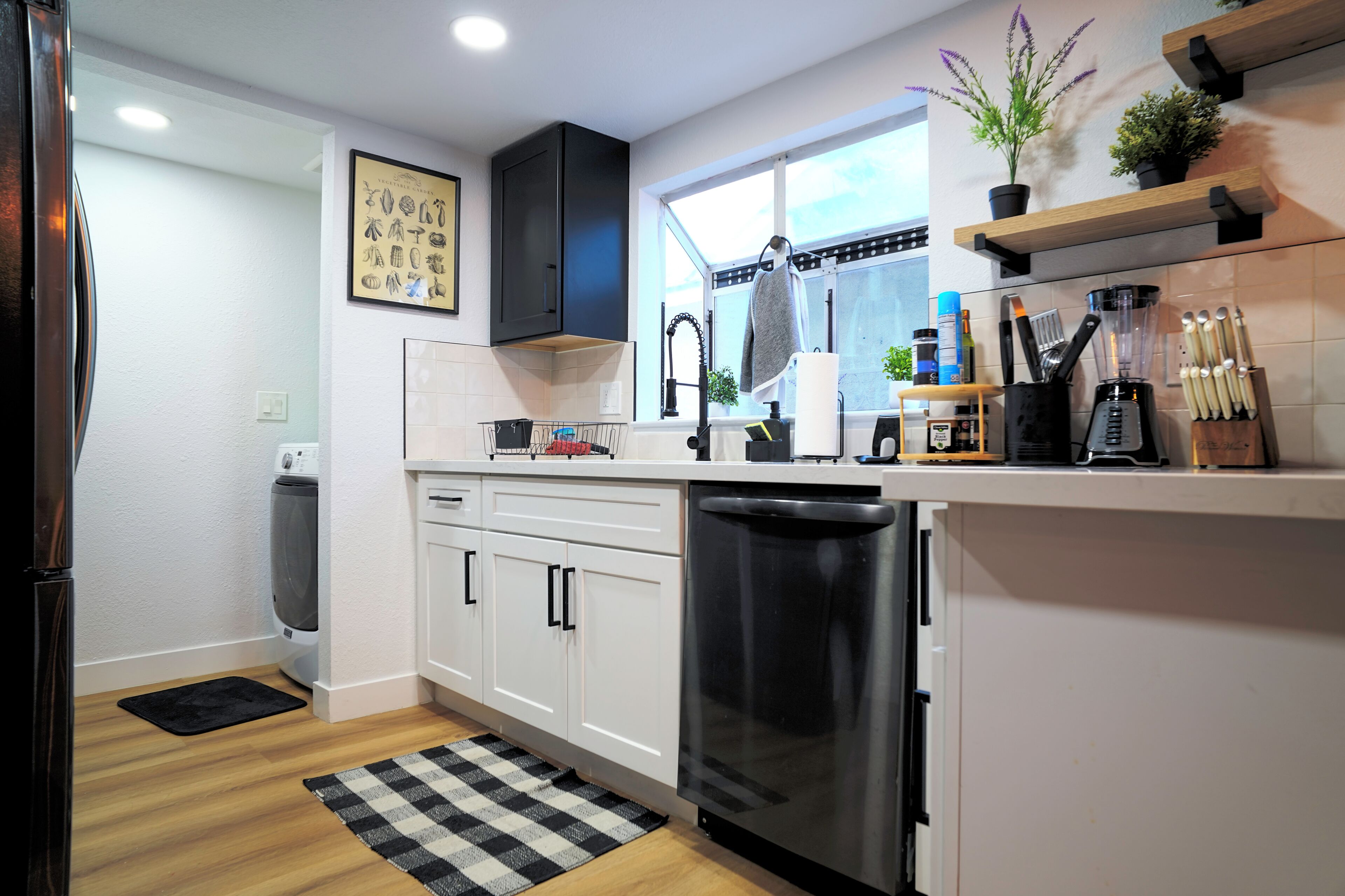 A modern kitchen with white cabinets, a dishwasher, a sink, and a window with a view.