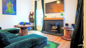 A living room with a fireplace, green sofas, a flat-screen TV, and a painting on the wall.