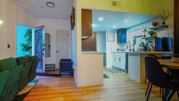 A modern kitchen with white cabinets, a dining area with a wooden table and chairs, and a living room with a green sofa.