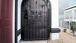 A black wrought iron gate with a decorative design, set in a white stucco wall with a red door to the left.