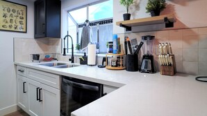 A modern kitchen with white cabinets, a built-in dishwasher, a window, and various kitchen utensils and appliances.