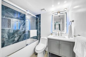 Un baño moderno con ducha de vidrio, inodoro blanco y tocador con espejo.