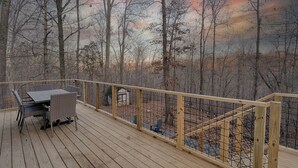 A wooden deck with a table and chairs, surrounded by a wooden railing and a view of a forested area.