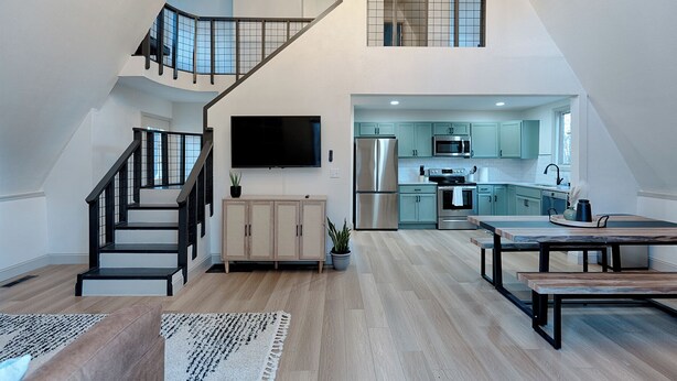 A spacious loft with a modern kitchen, a dining area, and a staircase leading to an upper level.