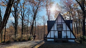 Una casa tradicional de entramado de madera con un tejado empinado, rodeada de un bosque.